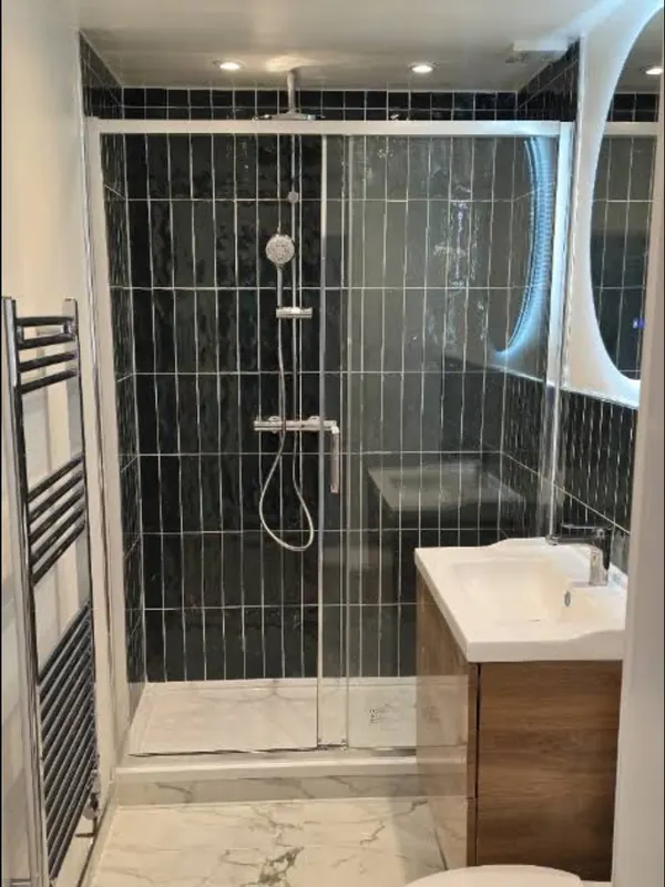 Shower room with dark wall tiles, glass enclosure, oak vanity unit and marble-effect floor